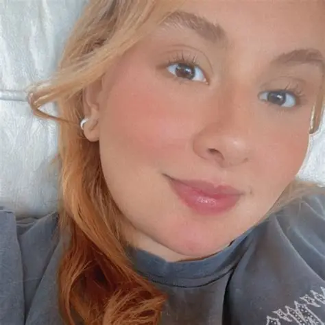 Smiling young woman with strawberry blonde hair and brown eyes wearing a dark grey t-shirt.