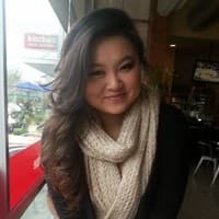 Smiling woman with long wavy brown hair wearing a cream knit scarf in a cafe.