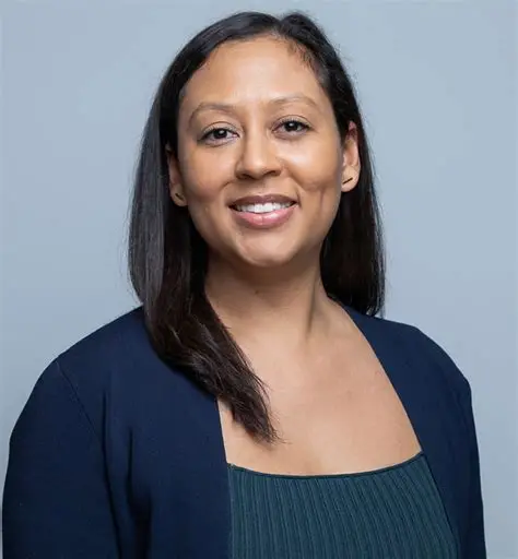 Professional headshot of a smiling woman with long dark hair wearing a navy blue blazer.