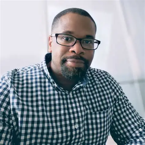 Black man with glasses and a goatee wearing a black and white checkered shirt.