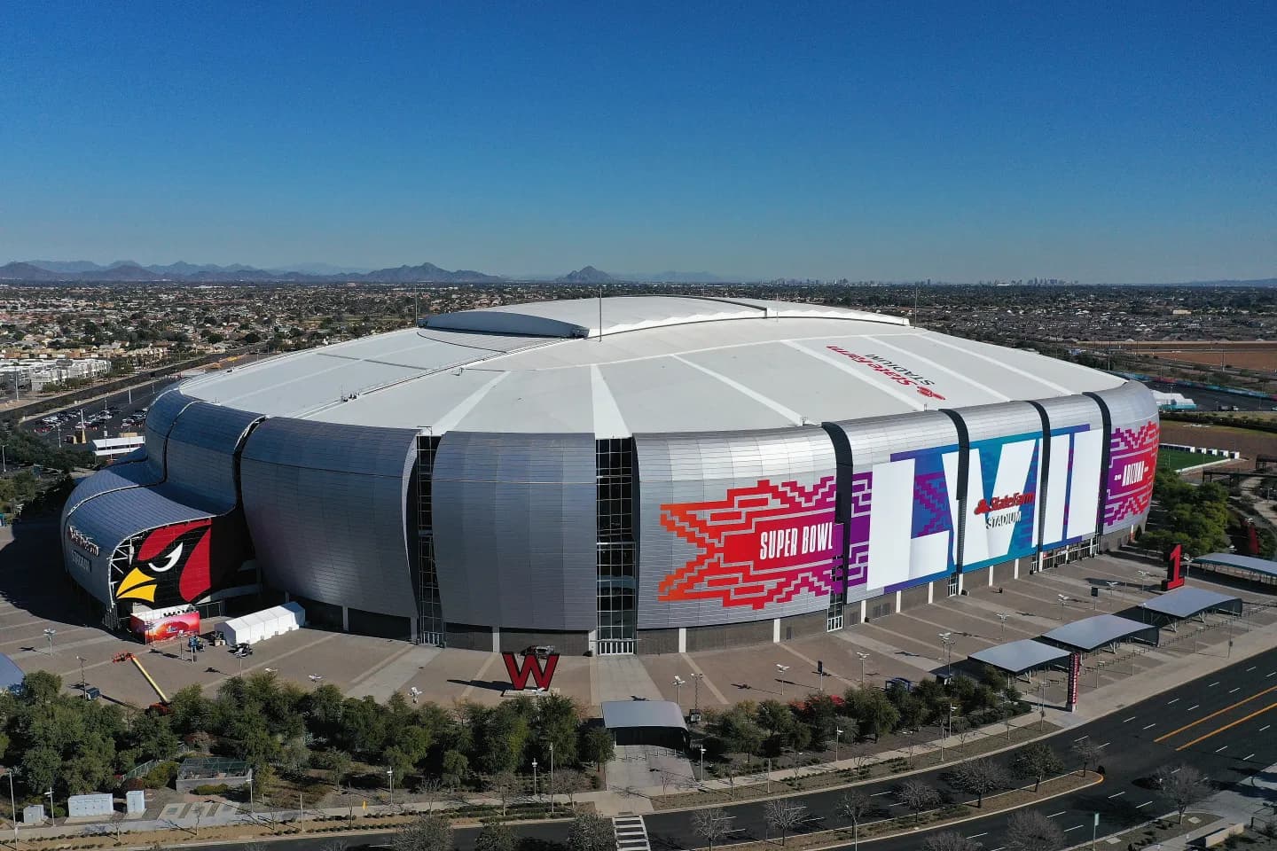 State Farm Stadium in Arizona decorated with Super Bowl LVII graphics under a blue sky.